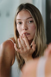 person applying naked tallow lip balm infront of the mirror