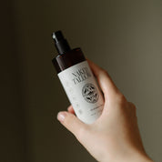 Hand holding a bottle of 'Naked Tallow' product against a neutral background