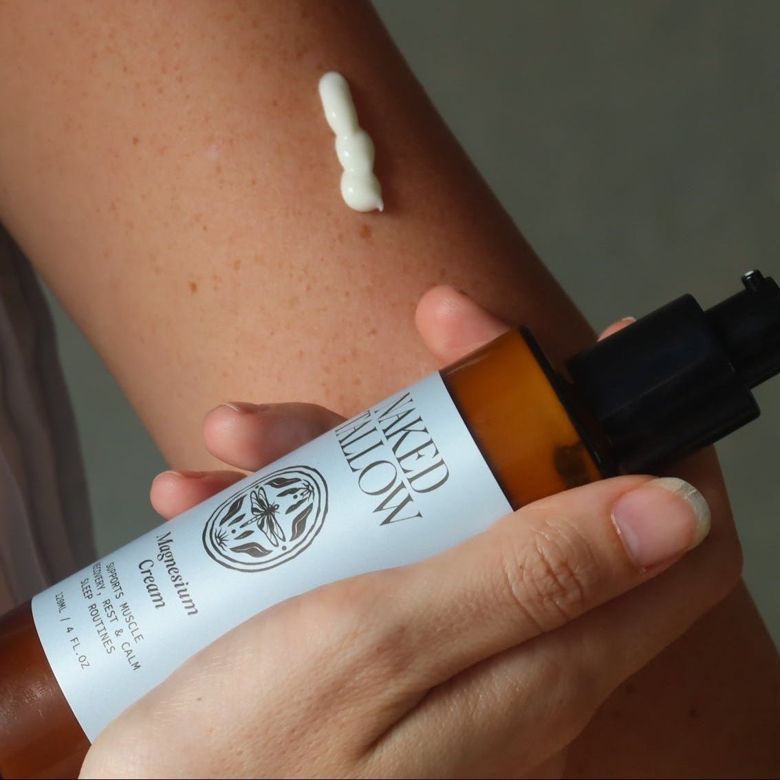 Person applying a white cream to their arm with a bottle labeled 'Naked Tallow.