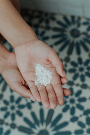 Hands holding a small amount of white powder on a patterned floor - Australian-made tallow skincare for deep yet gentle cleansing.