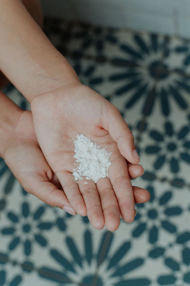 Hands holding a small amount of white powder on a patterned floor - Australian-made tallow skincare for deep yet gentle cleansing.