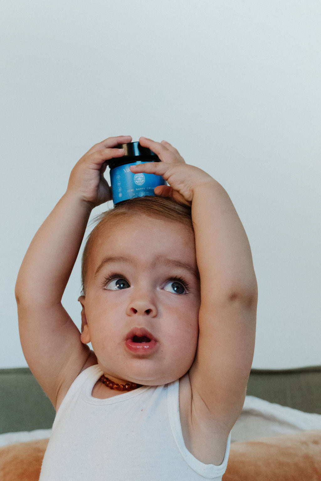 Baby holding a blue container above its head with a neutral background