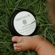 baby with jar of tallow balm in the grass