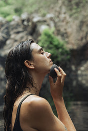 person using konjac sponge infront of waterfall with soap on face