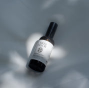 A bottle of Hydrating Mist by Naked Tallow, placed on a surface with a shadow falling over it.