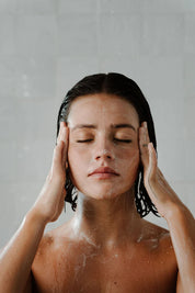 Woman with wet hair and soapy skin against a plain background - a fine, natural exfoliating powder for glowing, balanced skin, made with tallow and botanicals in Australia.