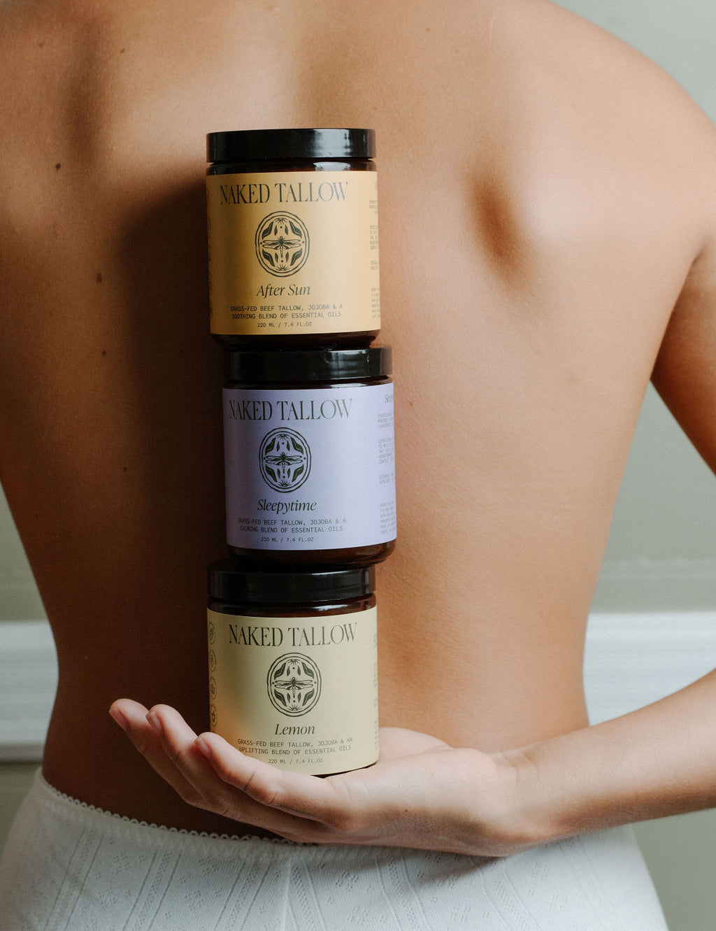 Three jars of scented tallow cream held in a person's hand, with labels indicating different scents.