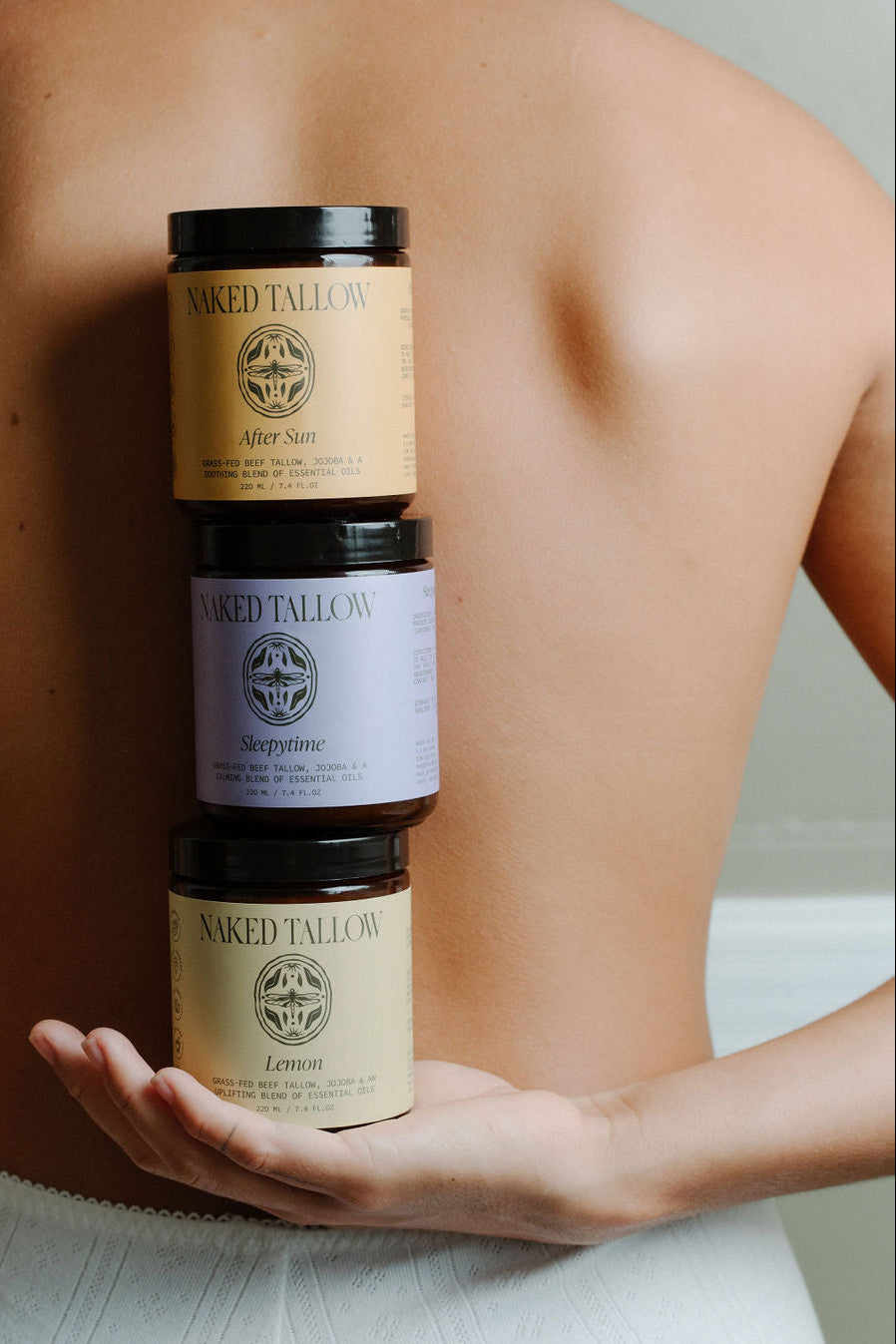 Three jars of scented tallow cream held in a person's hand, with labels indicating different scents.