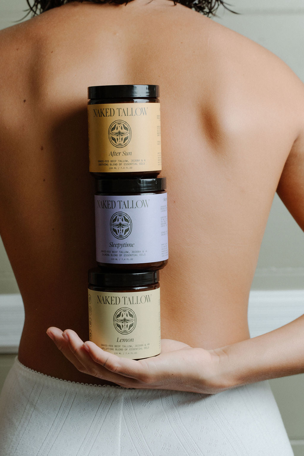 Three jars of scented tallow cream held in a person's hand, with labels indicating different scents.