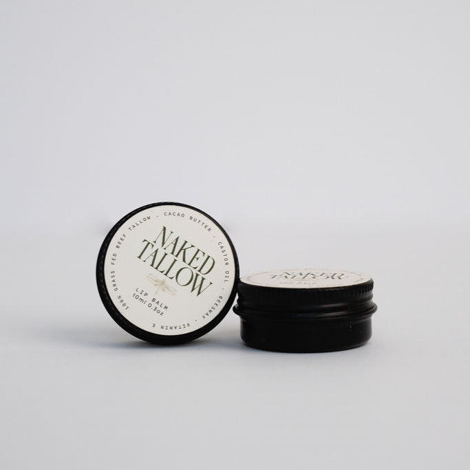 A stack of black lip balm containers with the top one lifted, revealing a white label with the brand name 'Naked Tallow' on it.