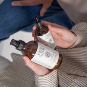 A person holding two bottles of skincare products, one labeled as 'VIBRANT OIL' and the other as 'Scented Tallow Cream', with the brand name 'Naked Tallow' visible.